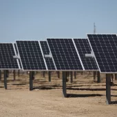 Rows of solar panels installed in a desert landscape under a clear blue sky, mounted on metal supports.