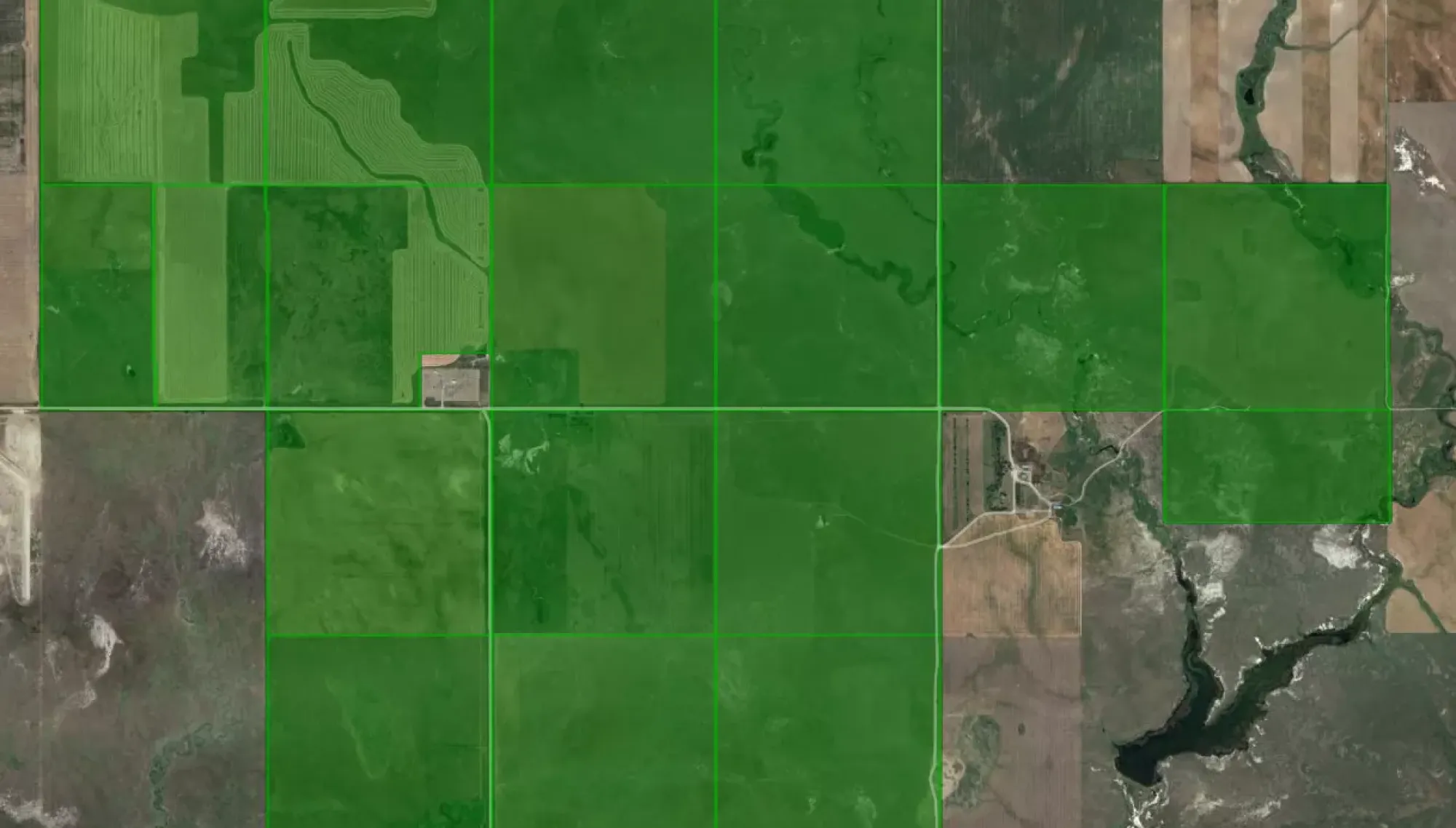 Aerial view of farmland divided into rectangular plots, highlighted in green. The plots contain various patterns of cultivation, surrounded by uncultivated land and a river running through the landscape.