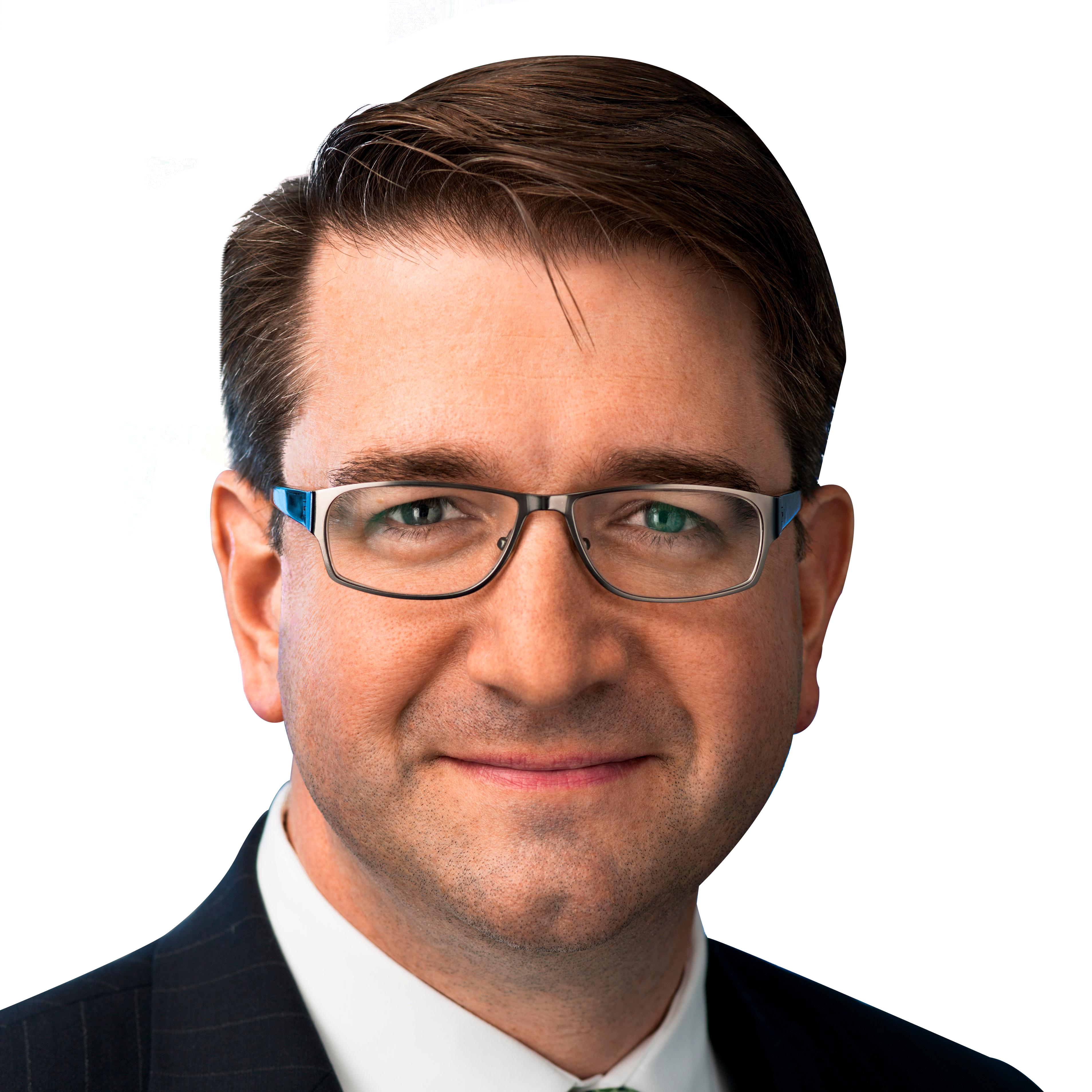 A man with short brown hair and glasses is wearing a dark suit and white shirt, smiling slightly against a black background.