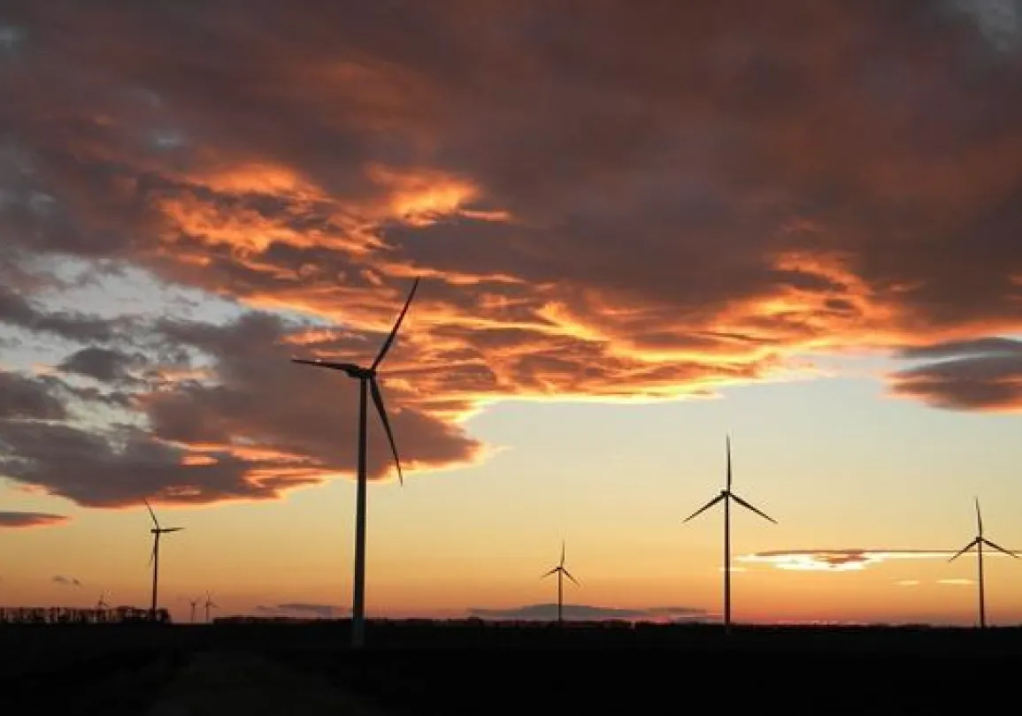 Silhouetted wind turbines against a dramatic sunset sky with orange and pink clouds.