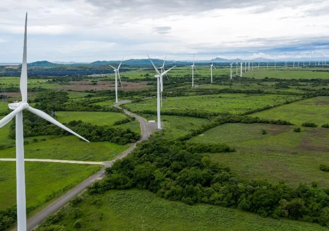 Aerial view of a wind farm with numerous wind turbines spread across a vast green landscape under a cloudy sky.
