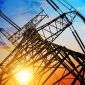 A silhouette of an electricity pylon against a vibrant sunset sky, with hues of orange, pink, and blue.
