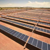Aerial view of a large solar farm with rows of solar panels on a dry, barren landscape under a clear sky.