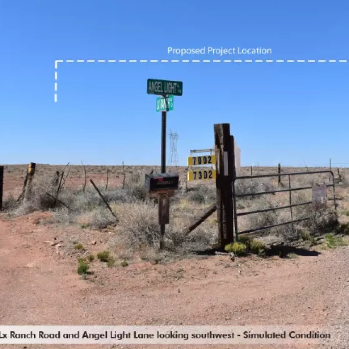 Rural intersection with dirt roads, a gate, and signs for Angel Light Lane and Lx Ranch Road. A dashed line indicates a proposed project location in the distance under a clear blue sky.