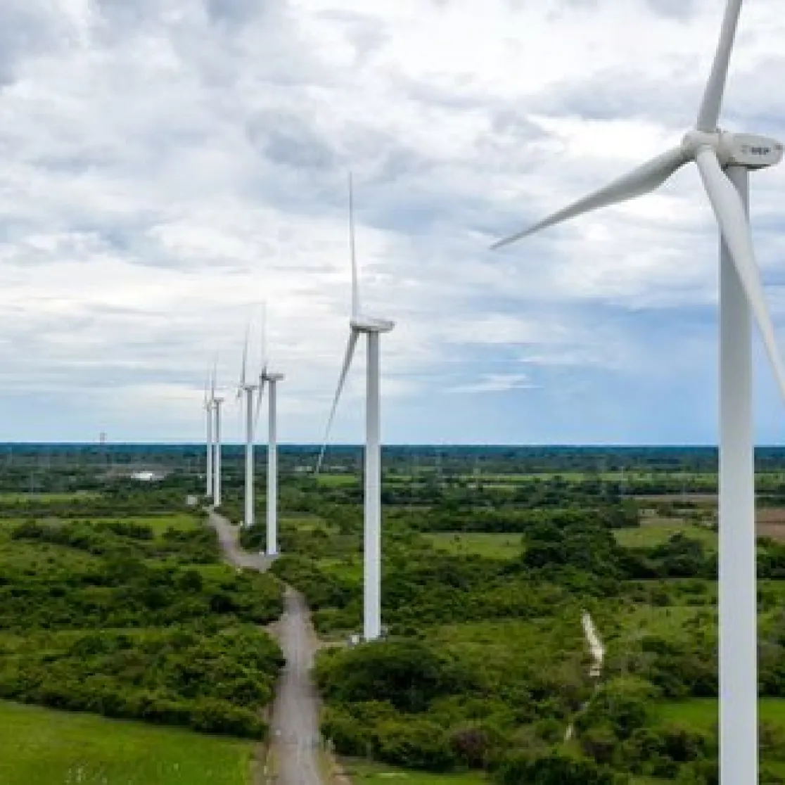 A row of wind turbines in a green landscape under a cloudy sky, generating renewable energy.