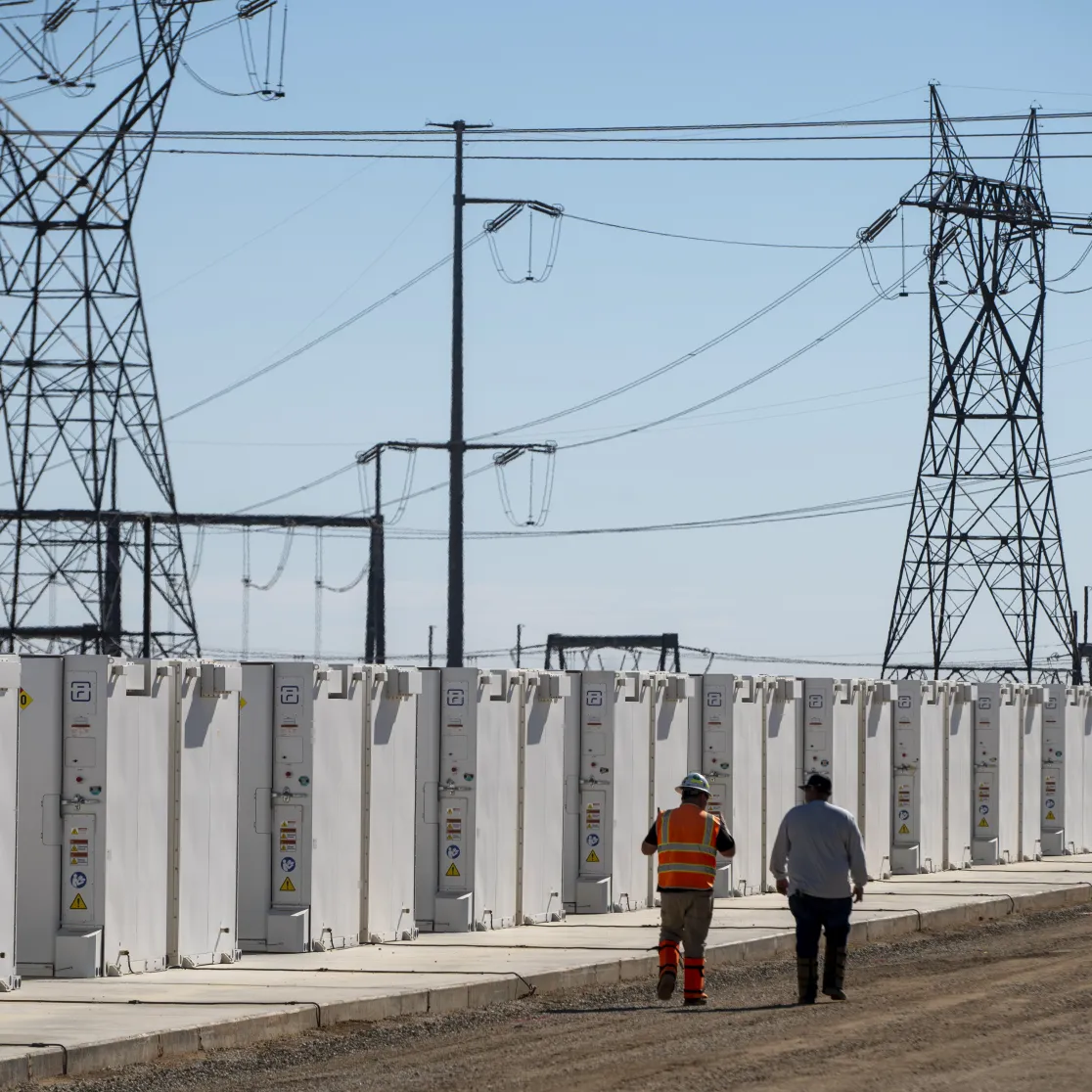 AES battery energy storage units in California with two workers walking beside the installation, high-voltage power lines overhead.
