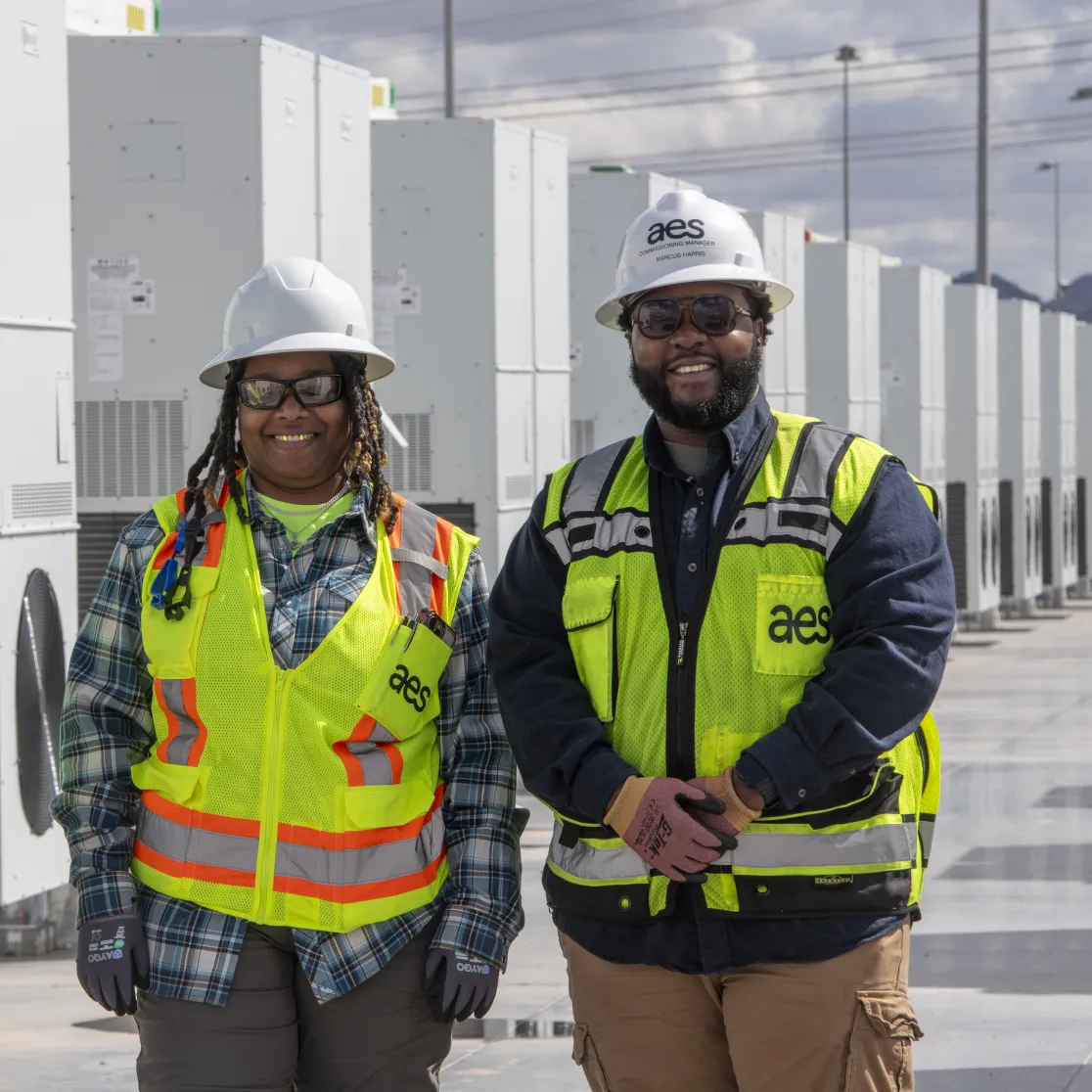 Two workers smiling in front of battery energy storage containers