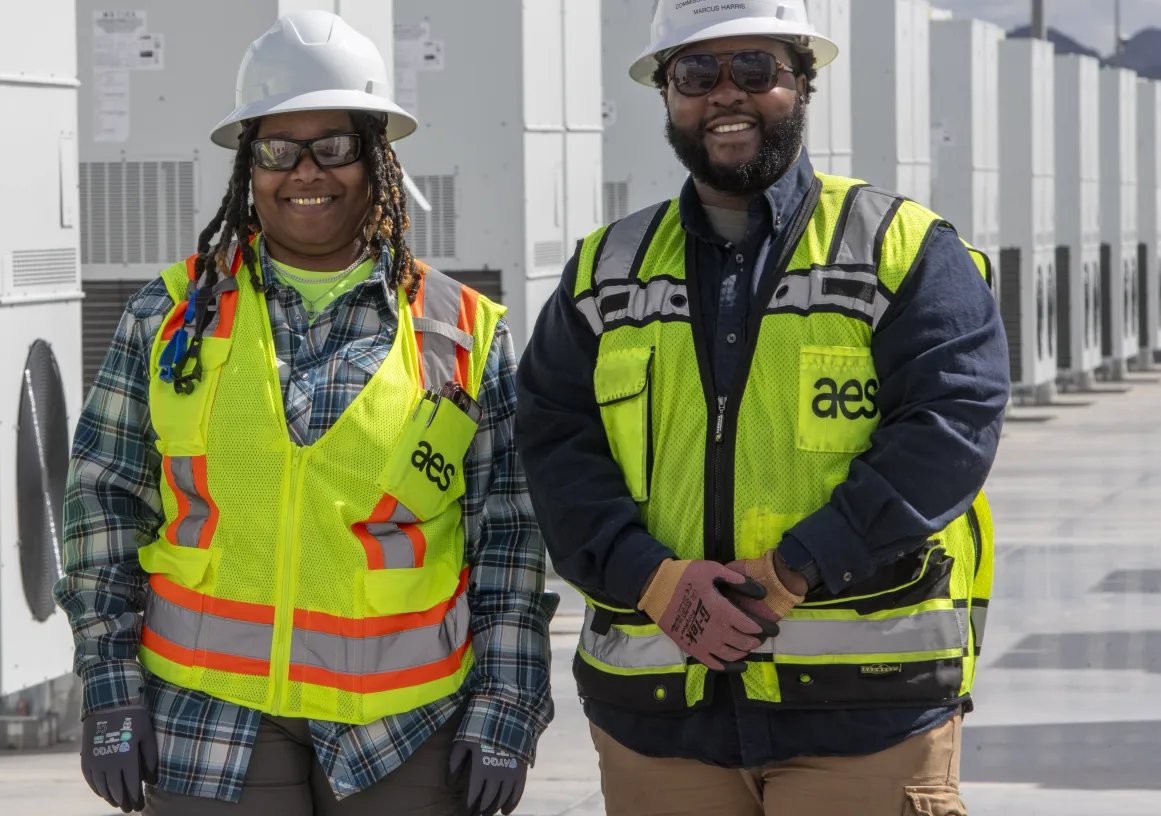 Two workers smiling in front of battery energy storage containers