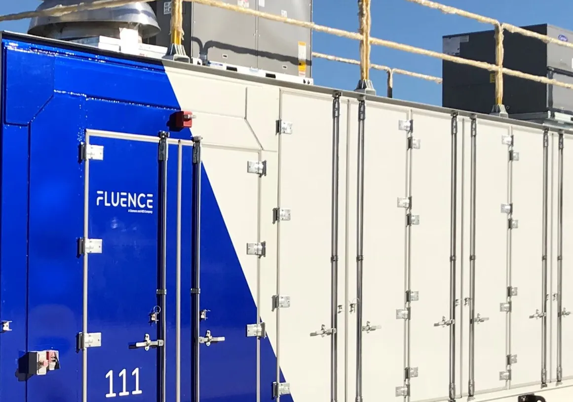 A large industrial container with a blue and white design labeled 'Fluence' and the number '111'. It has multiple doors and is situated outdoors under a clear blue sky.
