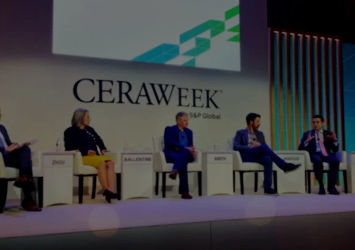 Five people sit on a panel stage at CERAWeek by S&P Global. They are seated in chairs with nameplates: Zhou, Ballentine, Smith, Manous, and Moreno. The backdrop features the CERAWeek logo and geometric designs. The panelists are engaged in discussion, with one speaking and others listening.