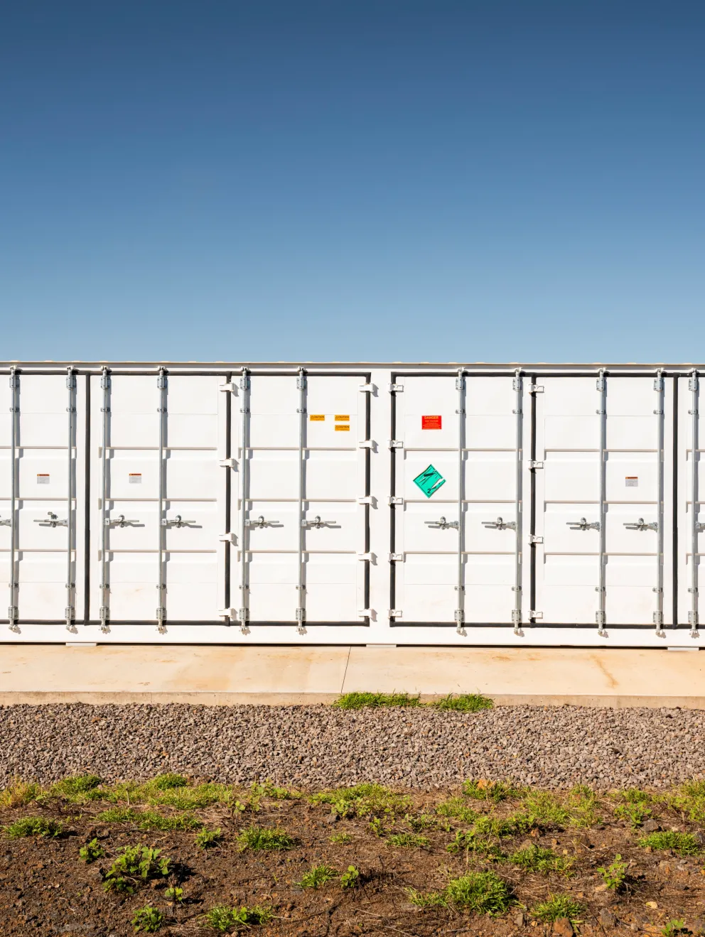 A large white shipping container with multiple doors and hazard symbols is positioned on a concrete platform. The sky is overcast.