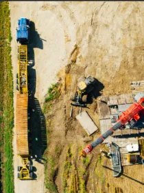 Aerial view of a construction site with machinery, including a red crane, surrounded by a field with green crops.