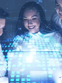 Three smiling professionals collaborate around a laptop with digital data graphics and blue network lines overlay, symbolizing teamwork and technology.