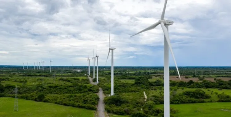 A row of wind turbines in a green landscape under a cloudy sky, generating renewable energy.