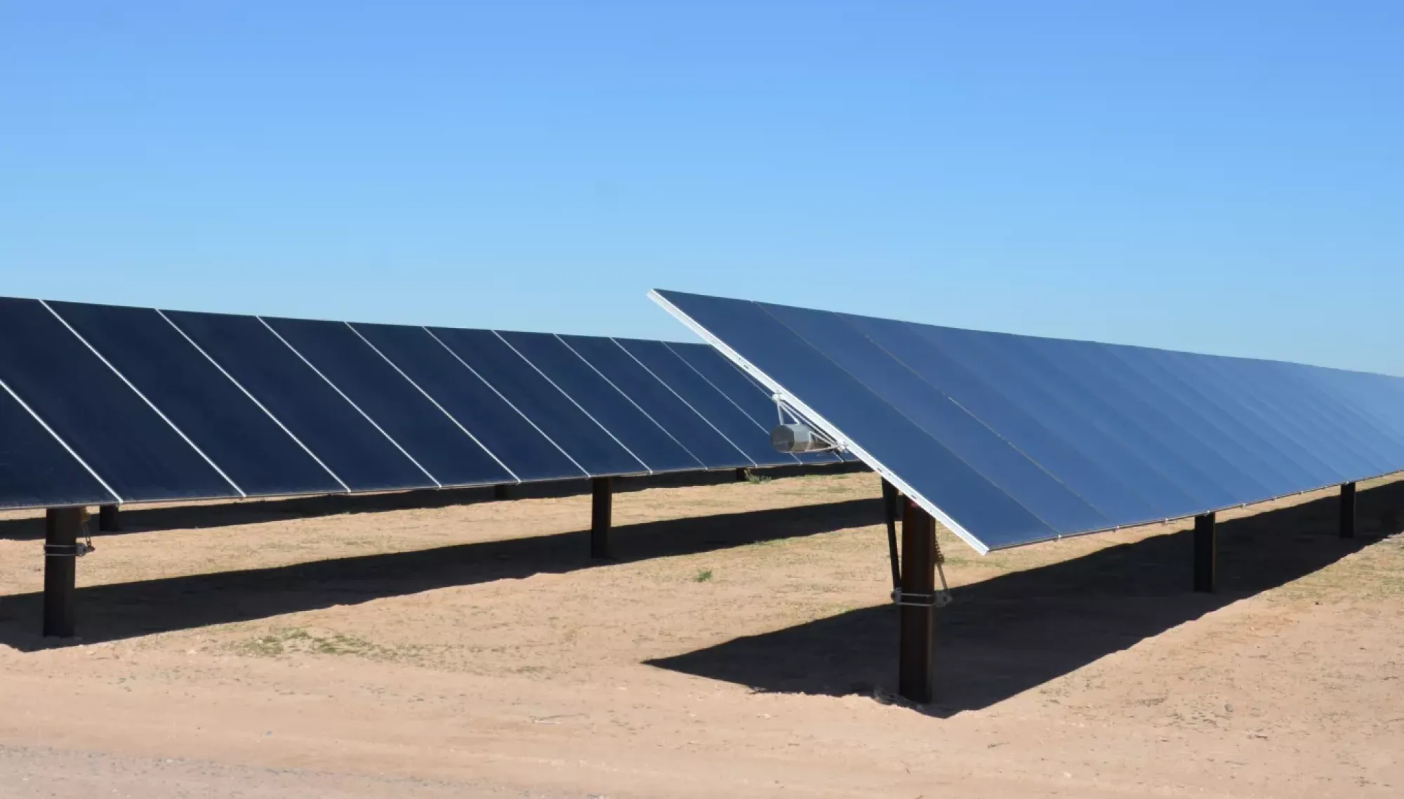 Rows of solar panels installed in a desert landscape under a clear blue sky.