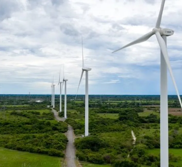 A row of wind turbines in a green landscape under a cloudy sky, generating renewable energy.