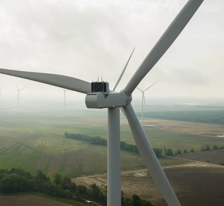 Close-up of a wind turbine in a field with several other turbines in the background under a cloudy sky.