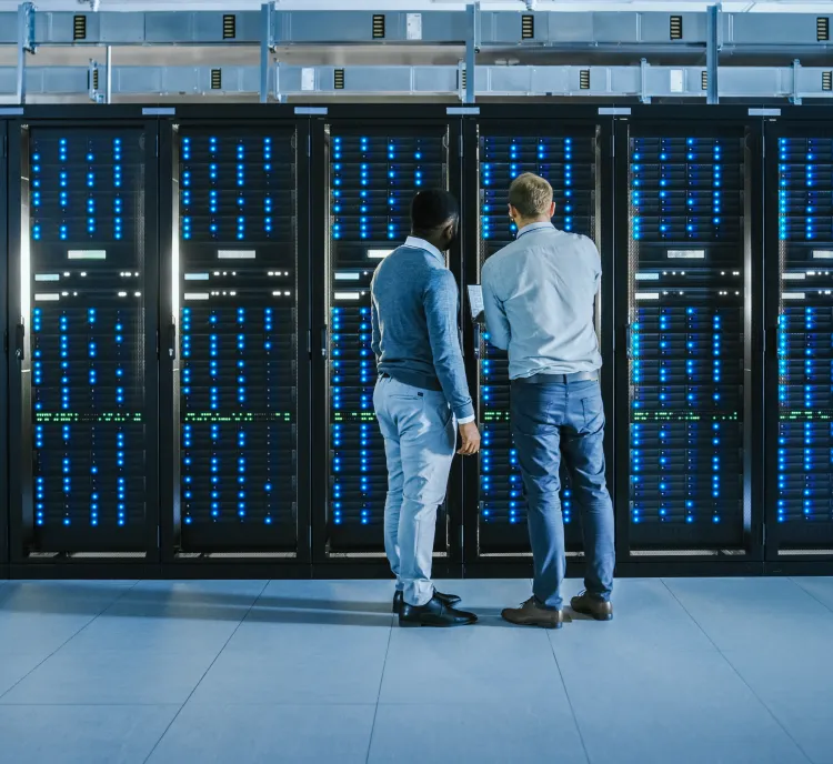 Two people standing in front of server racks with blue lights in a data center, examining equipment.