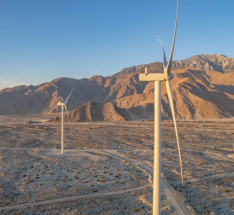 Aerial view of wind turbines in a desert landscape with mountains in the background under a clear blue sky.