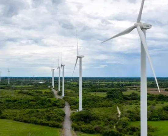 A row of wind turbines in a green landscape under a cloudy sky, generating renewable energy.