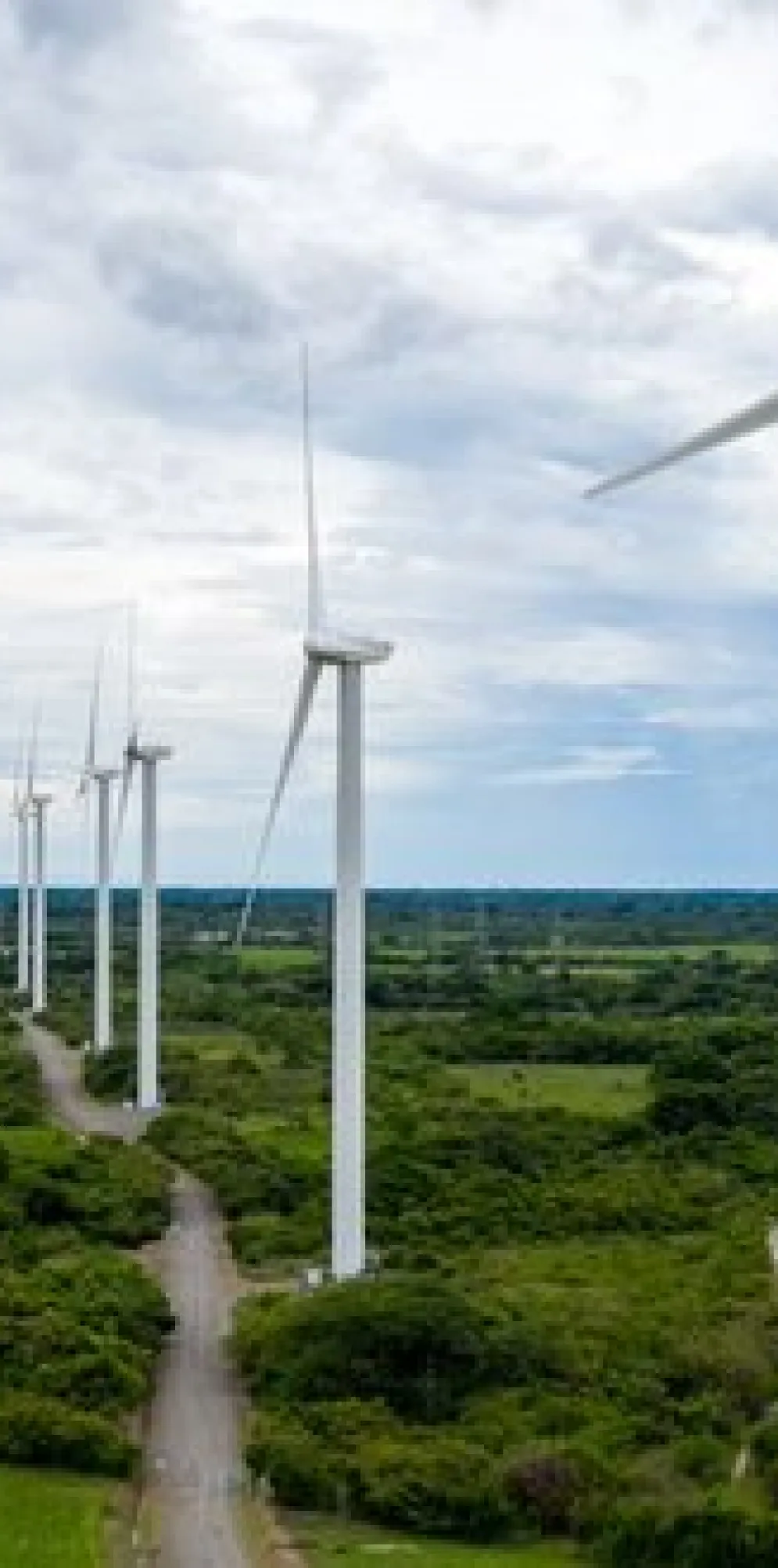 A row of wind turbines in a green landscape under a cloudy sky, generating renewable energy.