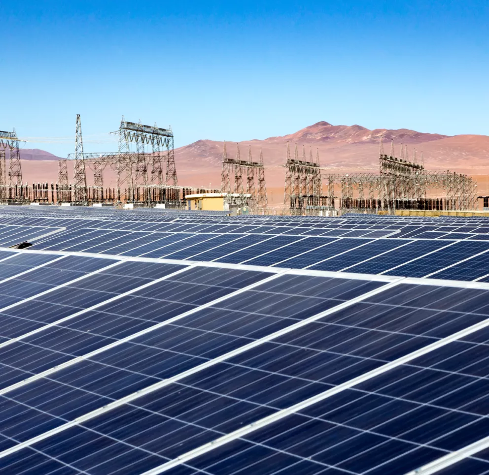 Large solar panel field with electrical substations in the background, set against a clear blue sky and desert landscape.