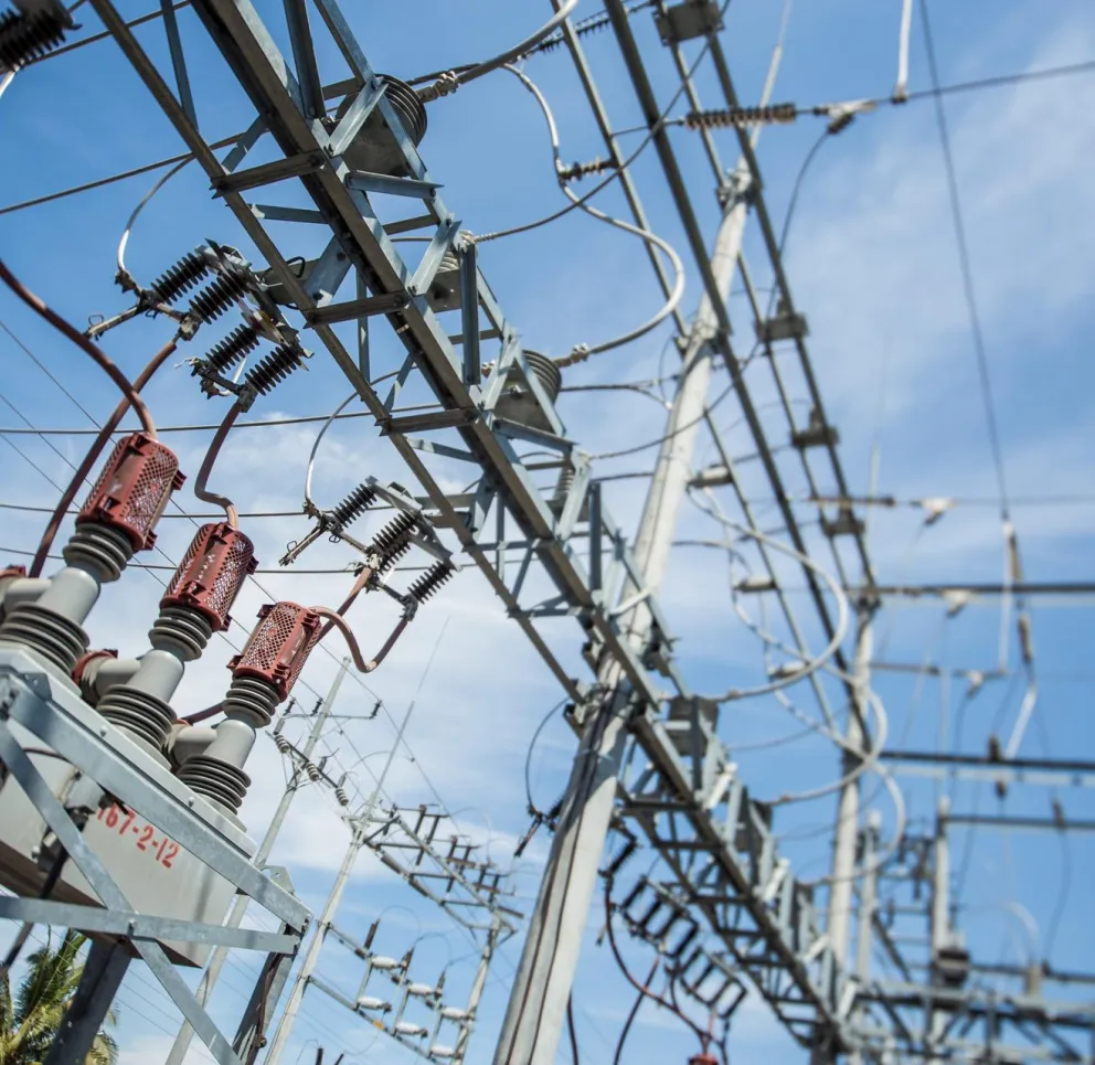 Close-up view of electrical substation equipment with transformers and power lines against a clear blue sky.