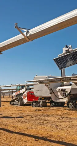 Three workers in safety gear stand near a solar panel installation site with a robotic vehicle on a sunny day.
