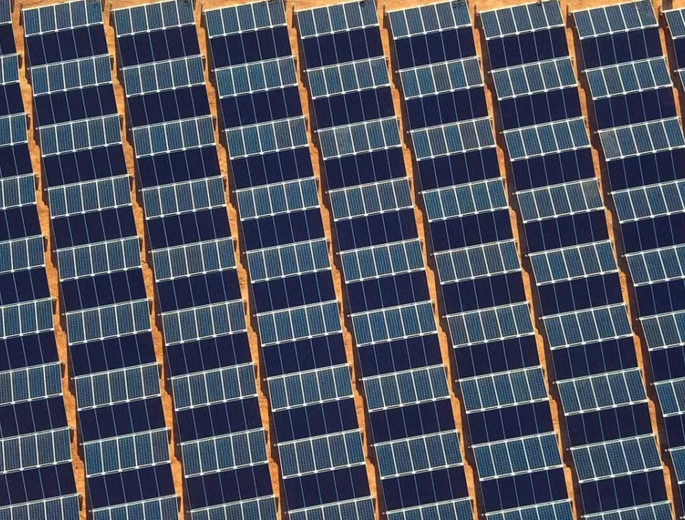 Aerial view of a solar panel farm with rows of solar panels on a dry, sandy landscape.