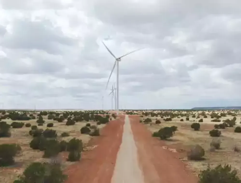 A dirt road leading to a series of wind turbines on a cloudy day in a desert landscape with sparse vegetation.