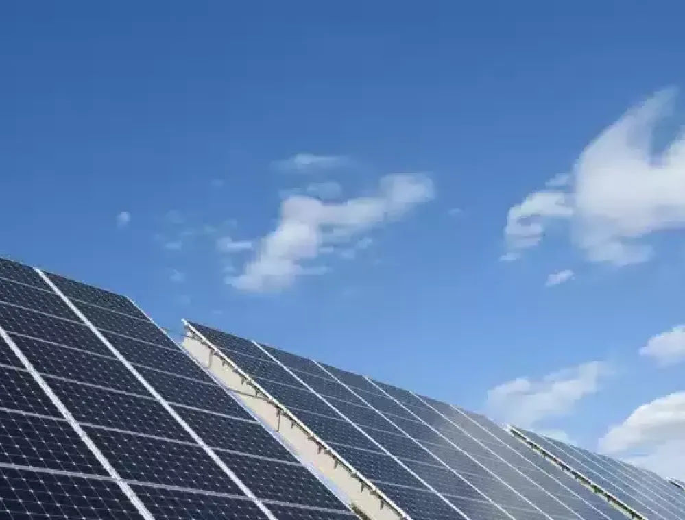 Solar panels under a clear blue sky with scattered clouds.