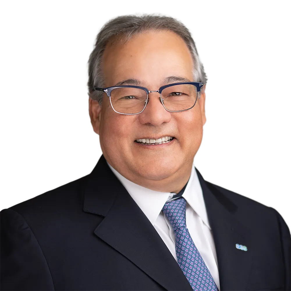 Smiling man wearing glasses and a suit with a blue tie, against a plain background.