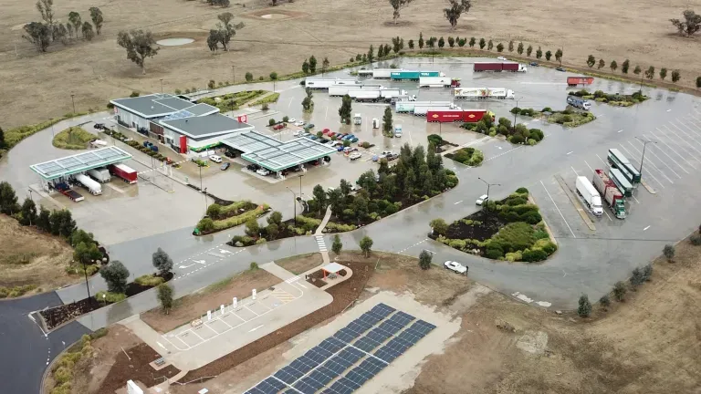 Aerial view of a roadside service station with multiple buildings, parked trucks, and a solar panel installation in a rural area.