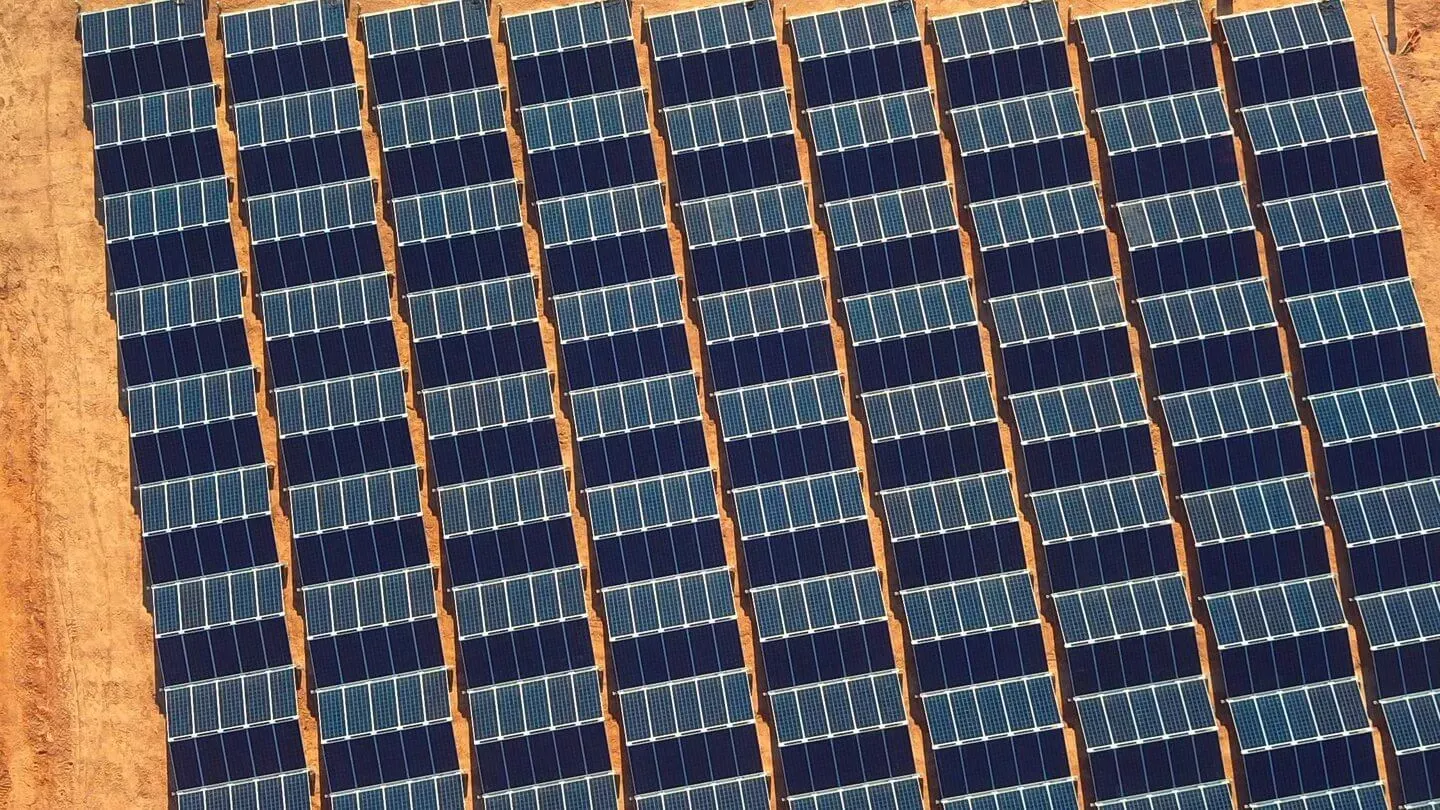 Aerial view of multiple rows of solar panels installed on a sandy ground, capturing sunlight for energy.