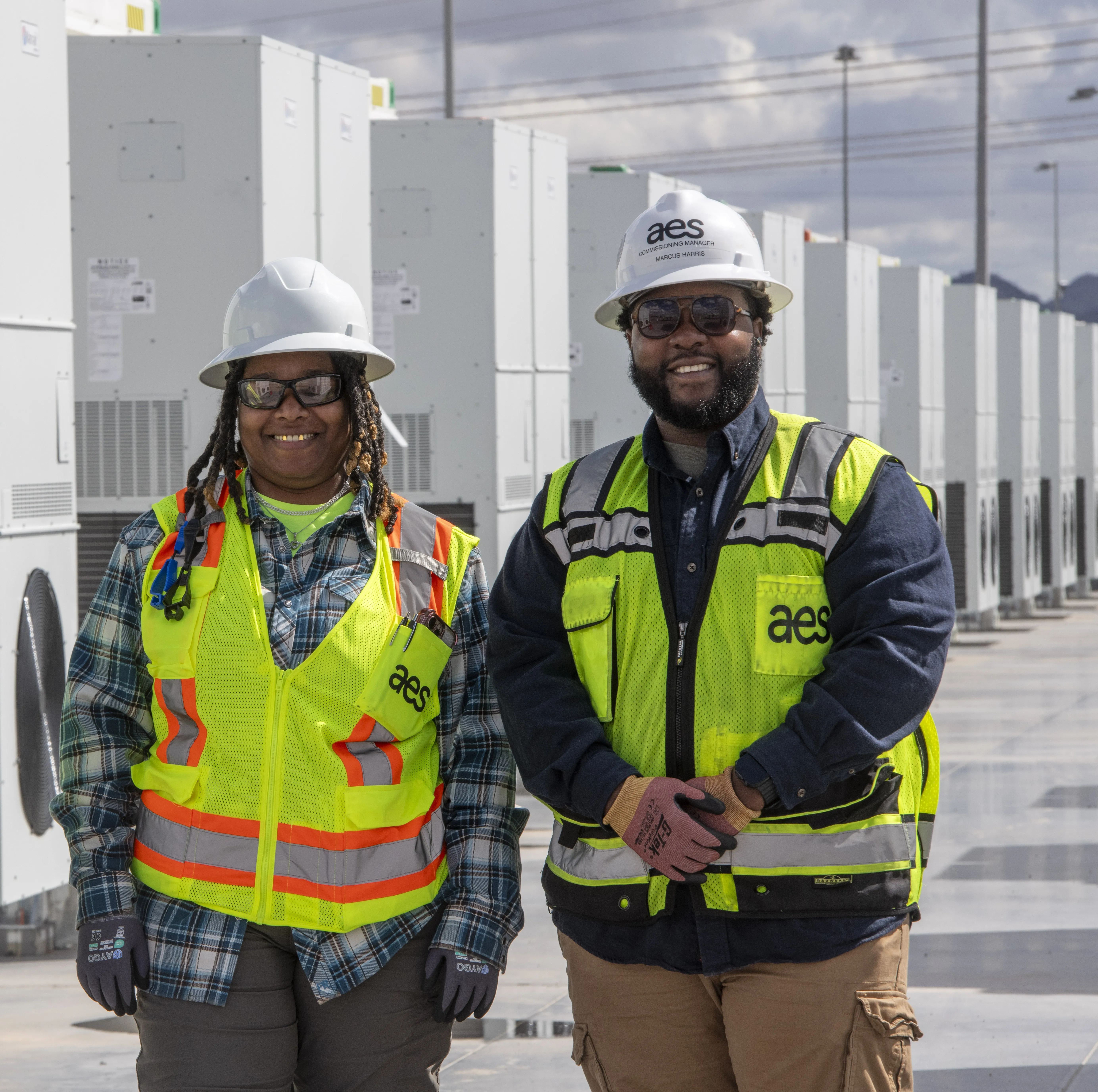 Two workers smiling in front of battery energy storage containers