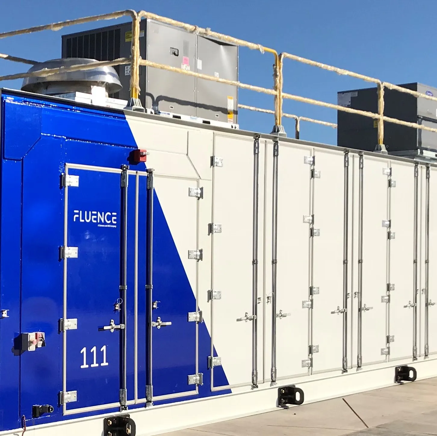 A large industrial container with a blue and white design labeled 'Fluence' and the number '111'. It has multiple doors and is situated outdoors under a clear blue sky.