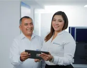 Two people in white shirts smiling and holding a tablet in an office setting.